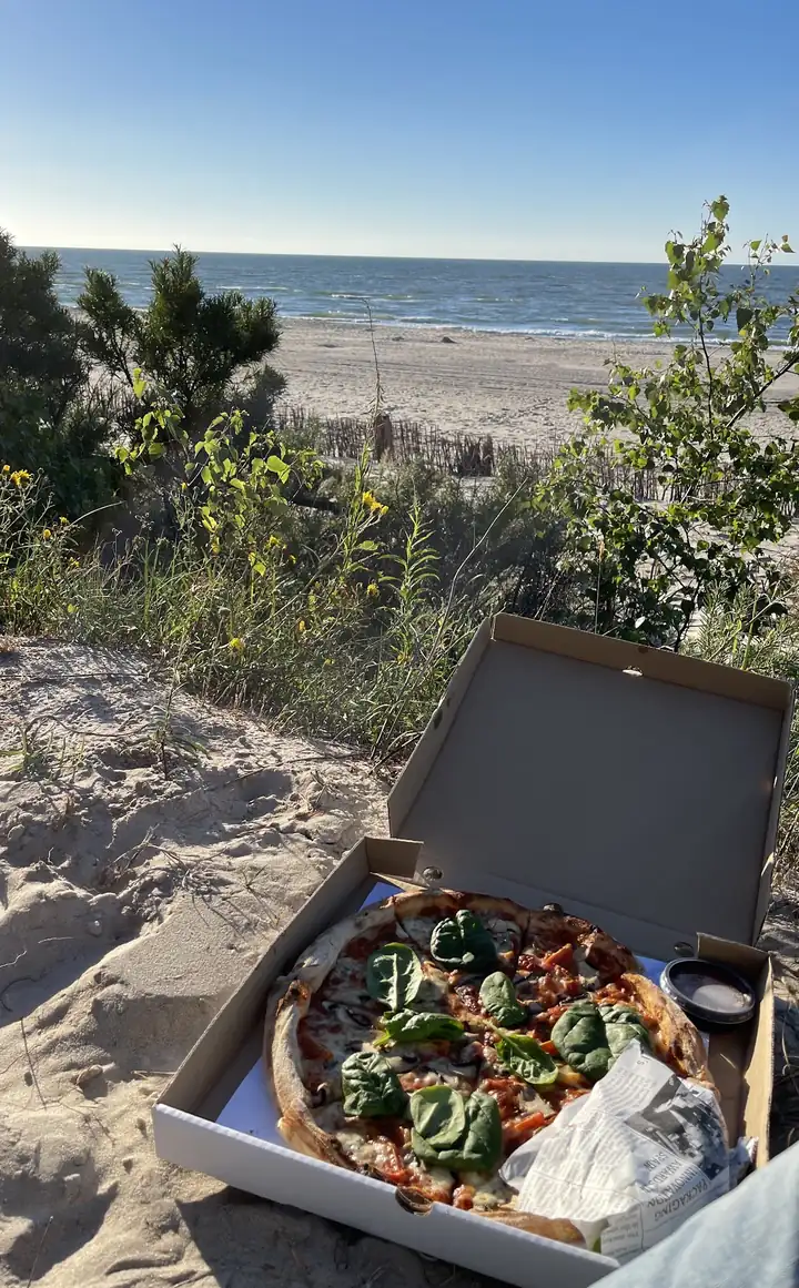Otwarty karton z pizzą Koni na wydmie, w tle Bałtyk
